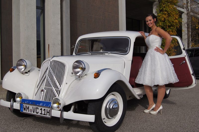 Braut im kurzen weißen Kleid an einem Oldtimer